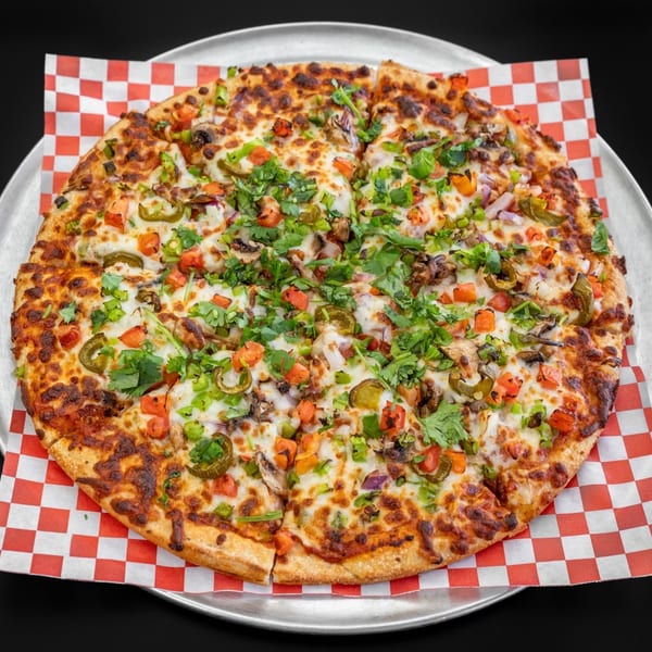 A whole pizza with melted cheese, tomatoes, jalapeños, onions, mushrooms, and cilantro on a metal tray.