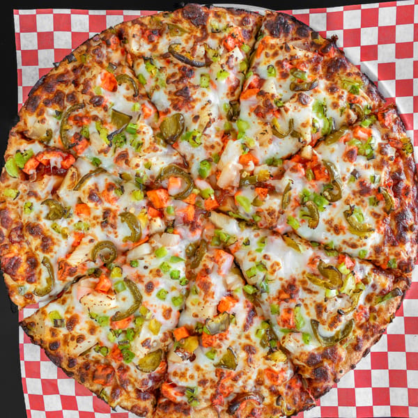 A whole pizza with melted cheese, chicken, green peppers, and onions on a red and white checkered paper.