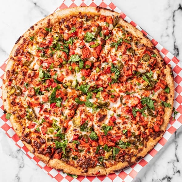 A whole chicken tikka pizza with cilantro and jalapeños on checkered paper.