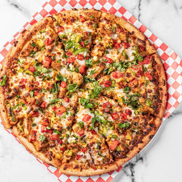 A whole pizza with chicken, bell peppers, tomatoes, and cilantro on a red and white checkered paper.